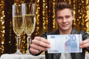 ragazzo mostra 20 euro e alle spalle due flute pieni di prosecco per il capodanno