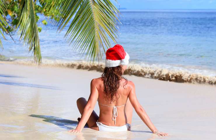 Donna in costume di spalle in spiaggia con cappello di Babbo Natale