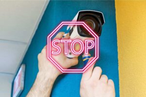 uomo installa una telecamera di sicurezza in condominio scritta stop in evidenza