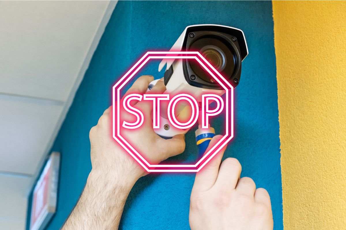 uomo installa una telecamera di sicurezza in condominio scritta stop in evidenza